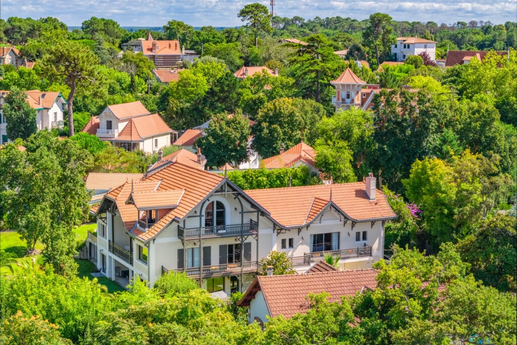 Villas de la Ville d'Hiver à Arcachon aux toits de tuiles rouges entourées d'une forêt dense sous un ciel d'été.