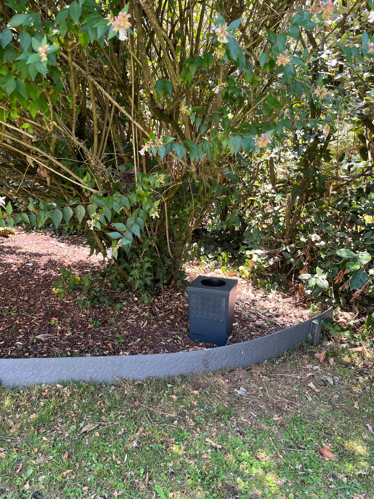 borne anti moustique Inyo installée sous un arbuste fleuri dans un jardin.